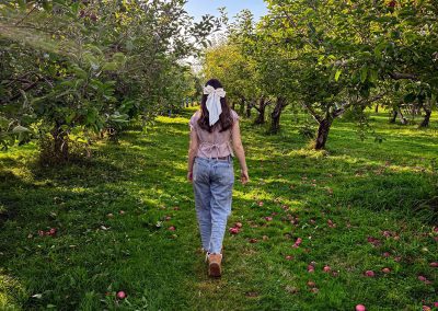 Girl with white bow in hair walking through apple orchard