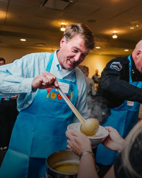 Former Mayor Tim Smith wearing a blue apron scooping soup into a bowl